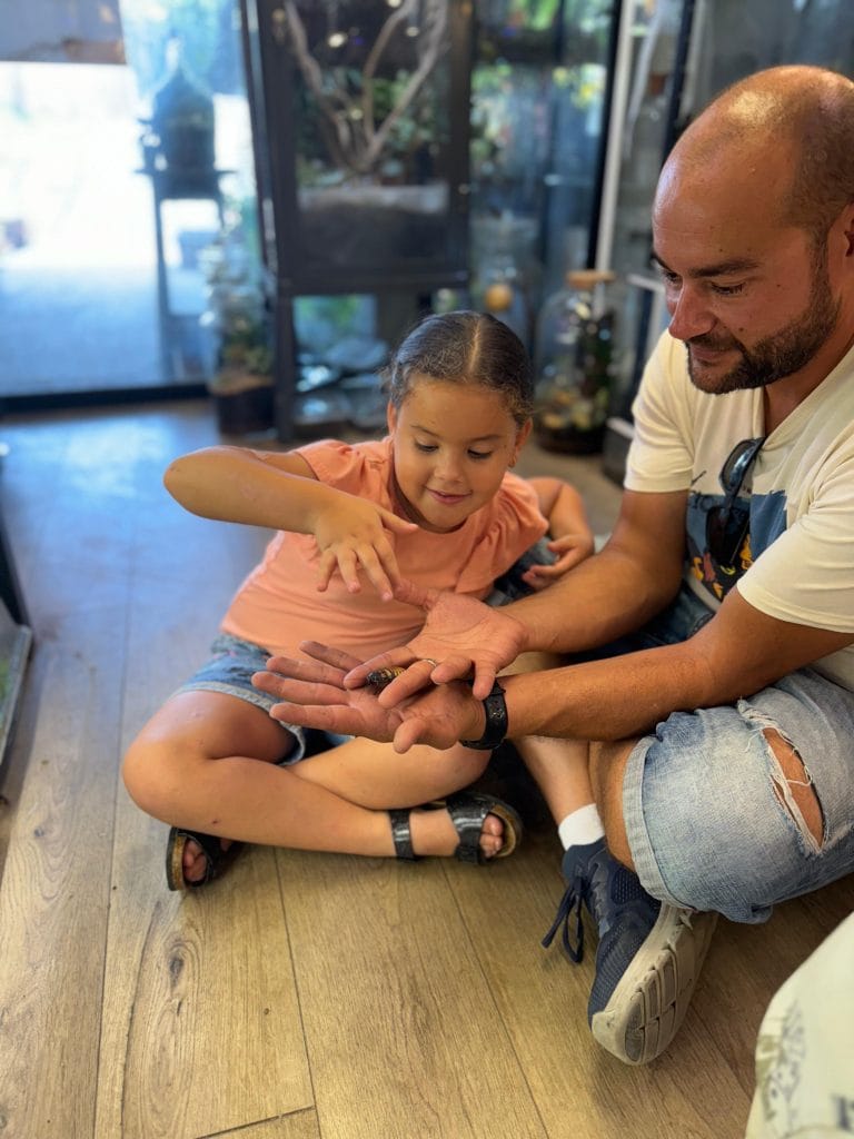 אב וילדה מחזיקים חרק על כף ידם בבית גידול לחיות מחמד.