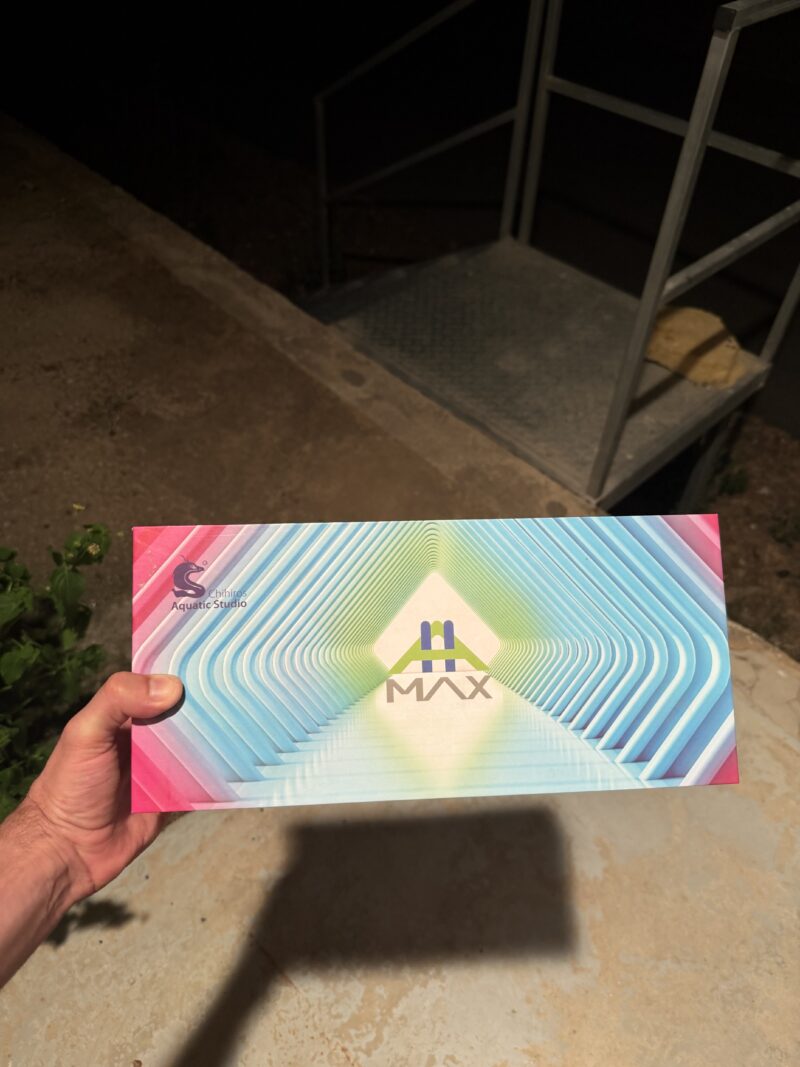 יד מחזיקה קופסת Chihiros Aquatic Studio MAX צבעונית בחוץ, רקע מדרגות.
