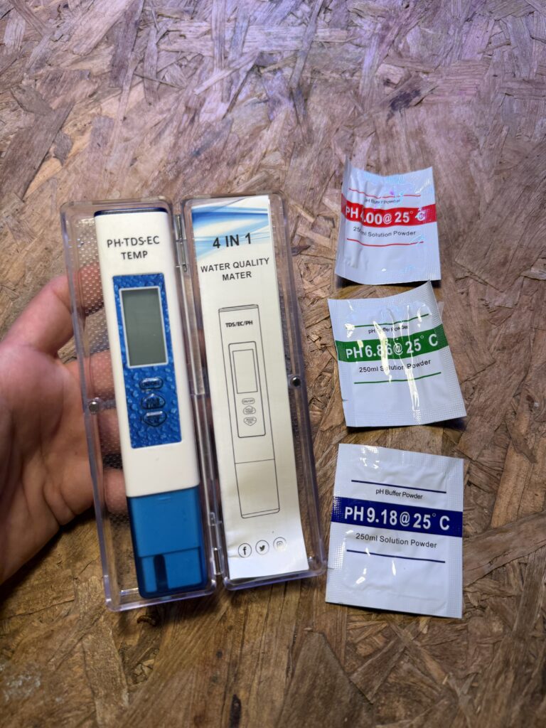 מד מים PH-TDS-EC-טמפרטורה, עם 3 אבקות בופר לכיול (PH4, PH6.86, PH9.18) על רקע עץ. מכשיר לבדיקת מים.