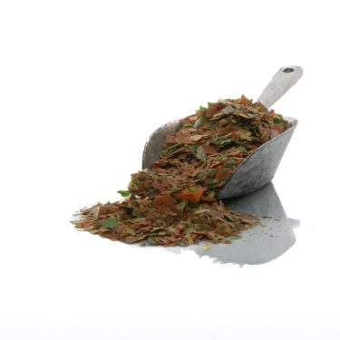 כף עם פתיתי מזון לדגים, חלקם נשפכים החוצה, על רקע לבן.